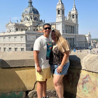 Couple posing in front of a historic building with domes and towers on a sunny day.