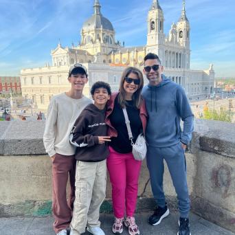 Four people smiling in front of a cathedral with towers and a dome on a sunny day.