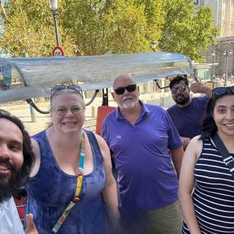 Group photo of five people smiling outdoors near trees and a building.