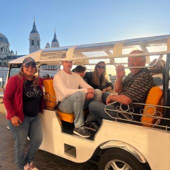 People sitting in an open-sided vehicle with a cityscape and blue sky background.