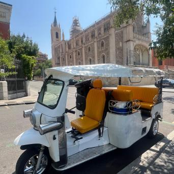 White tuk-tuk with orange seats parked near a historic church.