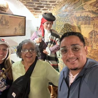 Three people smiling with a statue and wall map in background.