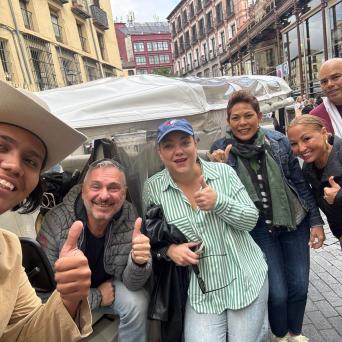 Group of people smiling and giving thumbs up on a city street.