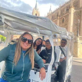 Four people in a tuk-tuk in front of an ornate historic building, smiling at the camera.