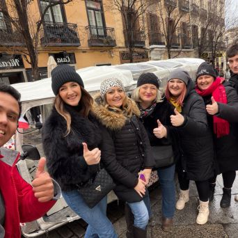 Group of people in winter clothes giving thumbs up on a street with buildings in the background.
