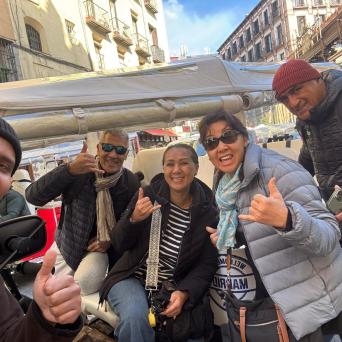 Group of five people smiling and giving thumbs up on a city street.