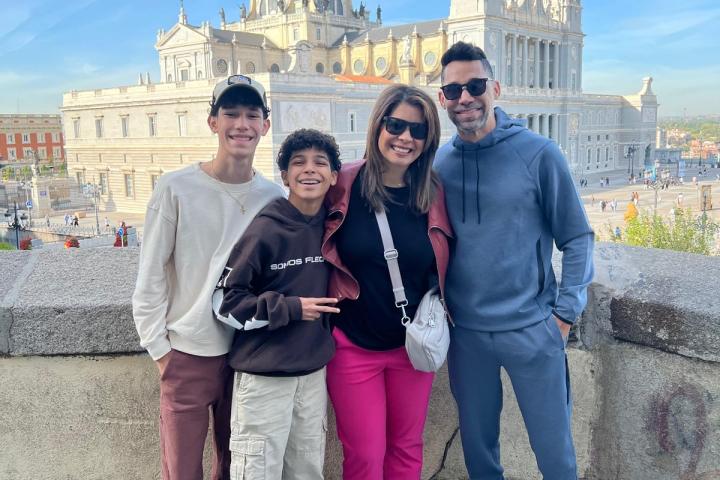 Four people smiling in front of a cathedral with towers and a dome on a sunny day.