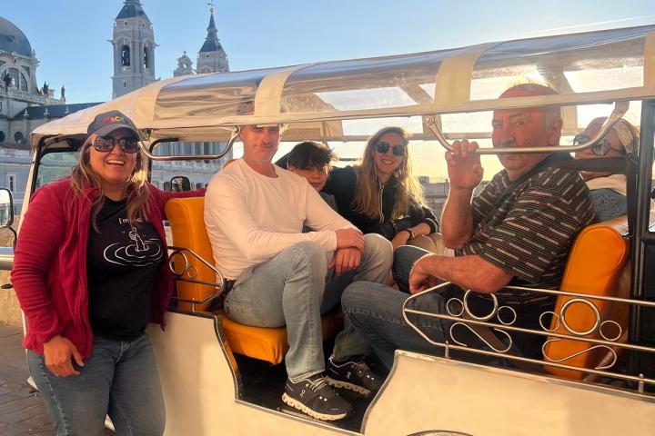 People sitting in an open-sided vehicle with a cityscape and blue sky background.