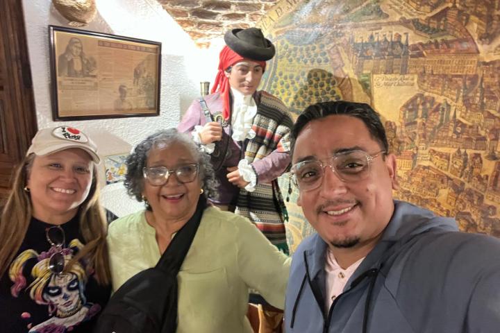 Three people smiling with a statue and wall map in background.