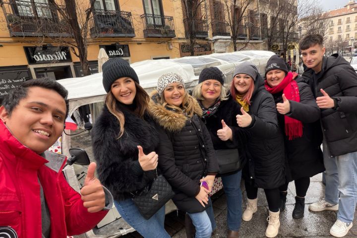 Group of seven people smiling and giving thumbs up outdoors on a rainy day.